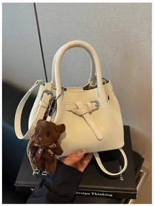 Nahaufnahme einer weißen Eimertasche mit Webmuster und einem braunen Bärenanhänger.