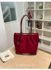 Détail d'un sac cabas en nylon rouge avec anses marron et breloque en forme de cœur