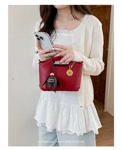 Stylish red leather handbag detail featuring decorative charms held by an Asian model