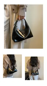 Detailaufnahmen einer schwarzen, glänzenden Achseltasche mit dekorativem Holzperlenanhänger.