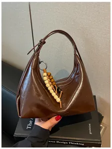 Nahaufnahme einer braunen glänzenden Schultertasche mit einem Holzperlen-Anhänger