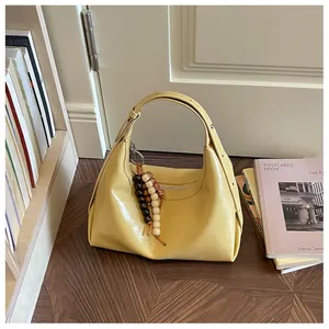 Elegante gelbe Hobo-Unterarmtasche mit stilvoller Perlenquaste in einer Lifestyle-Umgebung