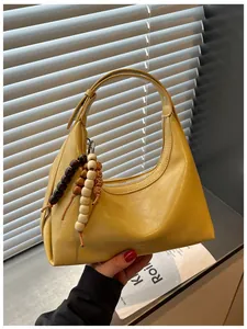 Detailansicht einer stilvollen gelben Hobo-Tasche mit einem Perlenanhänger.