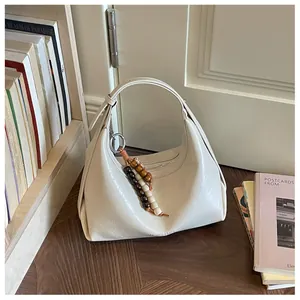 Detailansicht einer cremefarbenen Hobo-Schultertasche mit modischem Perlenanhänger.
