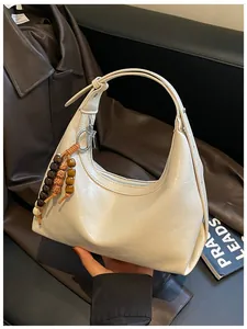 Detaillierte Nahaufnahme der cremefarbenen Hobo-Tasche mit dekorativem Holzperlen-Charm