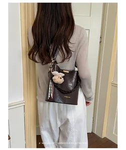 Rear view of a dark brown faux leather bucket bag with braided strap and plush charm