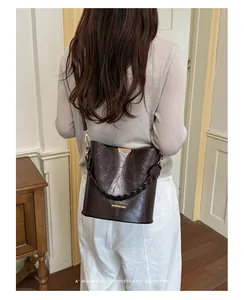 Dark brown glossy bucket bag with braided handle shown worn crossbody on a model