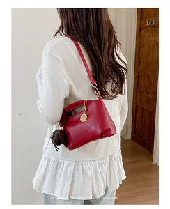 Detail view of a stylish red leather crossbody bag with gold accents worn by a model.