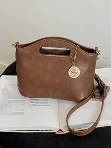 Vintage brown leather-style crossbody handbag with decorative gold charm pendant