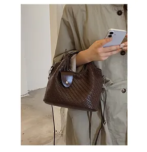 Detalle de un bolso cubo de tejido marrón oscuro combinado con una gabardina color caqui