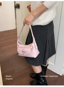 Close-up of a pink minimalist underarm bag worn with a white sweater and grey skirt.
