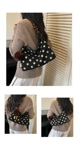 Detail of a chic black polka dot shoulder bag with unique wooden bead strap and pom-pom charm.