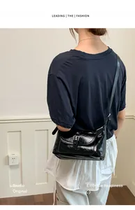 Fashionable shiny black leather crossbody shoulder bag worn by a model in a stylish outfit