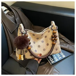 Close-up of suede-like polka dot handbag with wooden bead strap and pom-pom charm.