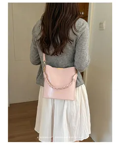 Elegant pink leather bucket bag shown as a crossbody on a model wearing a grey sweater