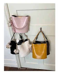 Four minimalist bucket bags in pink, white, black, and yellow hanging on a door