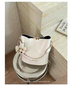 Elegant cream bucket bag detail with a cute teddy bear charm shown on a metal stool.