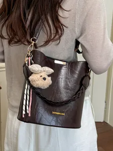 Elegant dark brown textured leather bucket bag featuring a cute plush bear charm for women