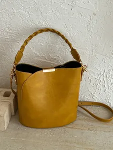 Stylish mustard yellow bucket bag with braided handle and gold-tone hardware detail.