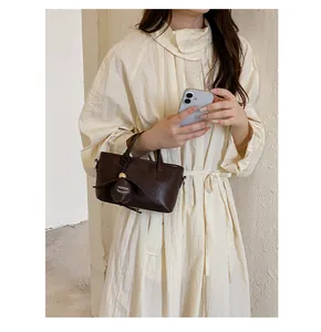 Gros plan d'un petit sac seau en cuir marron tenu par un mannequin en robe crème
