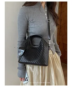 Primer plano de un bolso de cubo negro trenzado llevado por una modelo estilo retro.