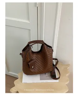 Detalle de un elegante bolso cubo trenzado marrón sobre una mesa auxiliar de madera.