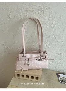 Detailed view of a stylish pink polka dot underarm bag with charms on a textured stone base