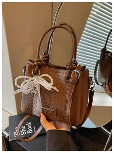 Vista detallada del bolso tipo cubo tejido marrón con lazo de perlas y encaje