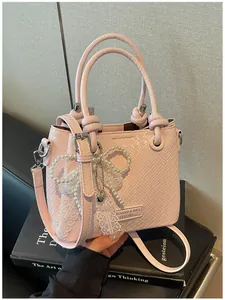 Elegante bolso de cubo rosa con textura tejida, lazo de perlas y encaje