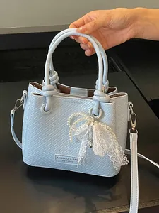 Bolso de mano azul claro con textura trenzada y colgante de lazo de perlas y encaje