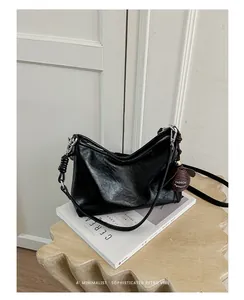 Borsa sottobraccio nera minimalista con ciondolo decorativo su rivista estetica.