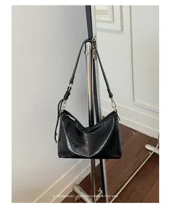 Dettaglio di una borsa sottobraccio in pelle nera lucida su un supporto di metallo