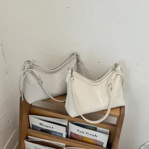 Eleganti borse sottobraccio da donna color crema e bianco su un portariviste in legno.
