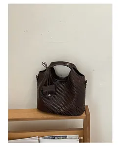 Vista detallada de un bolso de mano tipo bombonera tejido marrón para mujer en estante