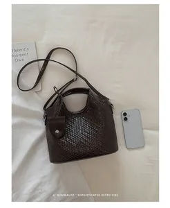 Primer plano de un bolso de cubo trenzado marrón oscuro junto a un teléfono inteligente