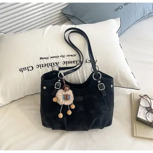Bolso tote retro negro mate de gran capacidad con colgante de peluche en una cama