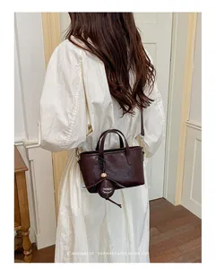 Vue détaillée d'un sac seau marron foncé sophistiqué porté par un mannequin en robe crème
