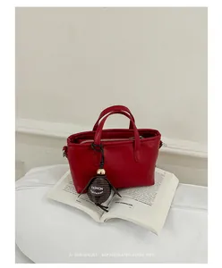 Détail d'un mini sac seau rouge avec un pendentif mode posé sur un livre ouvert