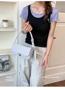 Close-up of a stylish grey baguette shoulder bag worn by a model in a cozy room