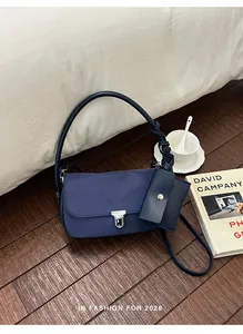 Elegante borsa a tracolla baguette blu navy con mini pochette coordinata su pavimento in legno