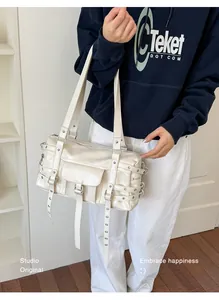 Close-up of cream rivet shoulder bag with multiple buckles and grommet straps