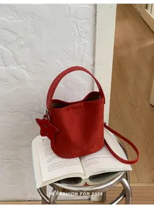 Détail d'un sac seau élégant en daim rouge avec breloque étoile posé sur un livre