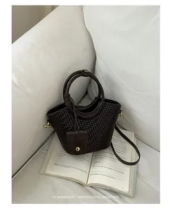Détail du sac seau tressé marron foncé sur un canapé blanc avec un livre