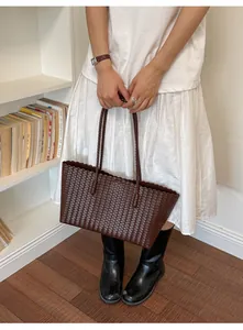 Borsa tote in pelle intrecciata marrone scuro tenuta da una modella in abiti casual