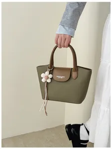 Stylish green canvas handbag with brown leather trim and flower charm held by a woman.