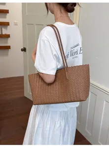 Vista laterale di una borsa tote in pelle intrecciata marrone indossata da modella