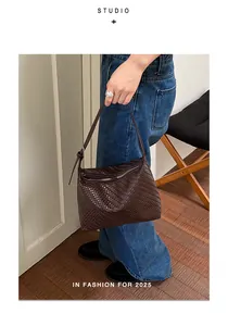 Close-up of a dark brown woven shoulder bag held by a person in a lifestyle setting