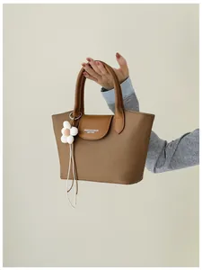 Close-up of a vintage brown canvas handbag with leather flap and white flower charm detail