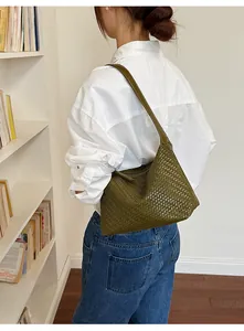 Close-up detail of the green woven underarm shoulder bag worn by a model in a library