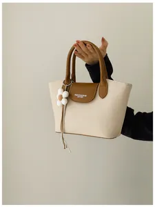 Close-up of a stylish canvas tote bag featuring brown leather trim and a flower charm